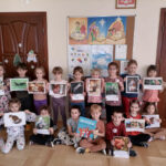 – Na zdjęciu widoczna jest grupa 16 przedszkolaków (11 dziewczynek i 5 chłopców) pozujących do wspólnego zdjęcia. 9 przedszkolaków stoi a 7 siedzi na podłodze, 2 chłopców trzyma książkę, a pozostałe dzieci trzymają zdjęcia wiewiórek.