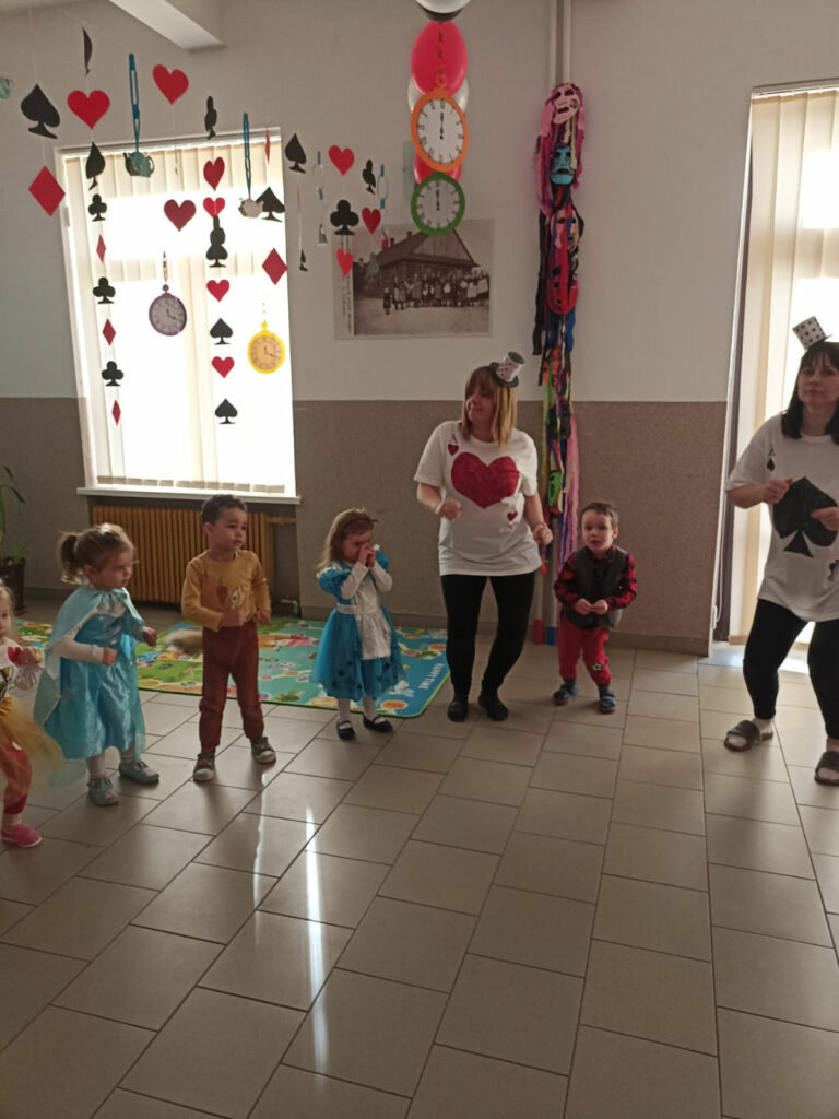 Na zdjęciu widoczna jest grupa przedszkolaków i 2 panie podczas zabawy w kaczuszki. W tle dekoracje tematyczne.