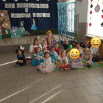 Na zdjęciu widoczna jest grupa przedszkolaków i pani wychowawczyni pozujących do wspólnego zdjęcia. W tle dekoracje tematyczne.