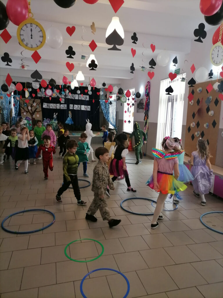 Na zdjęciu widoczna jest grupka przedszkolaków biorących udział w zabawie „wędrujące bransoletki”. W tle dekoracje tematyczne.