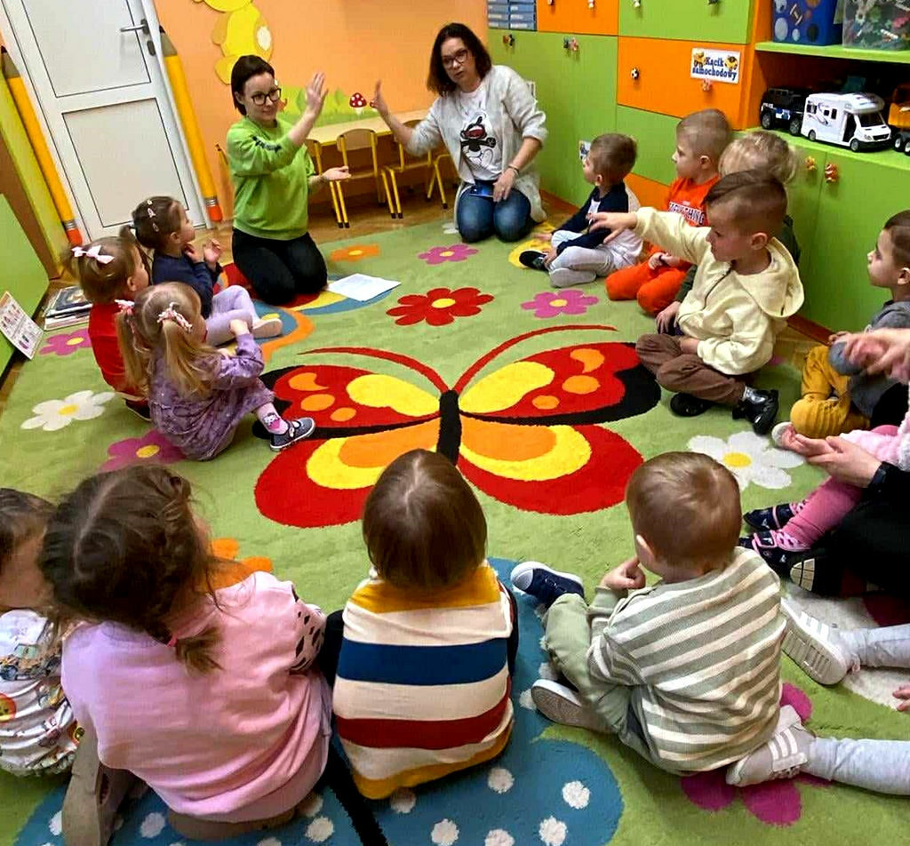na zdjęciu widać dzieci siedzące na kolorowym dywanie