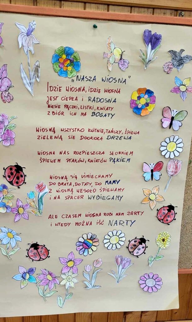 na zdjęciu widać arkusz papieru i napisany na nim wiersz ozdobiony pomalowanymi przez dzieci kwiatkami
