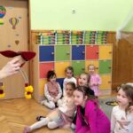 na zdjęciu widać dzieci siedzące na dywanie i pokazującą im maskotkę kobietę