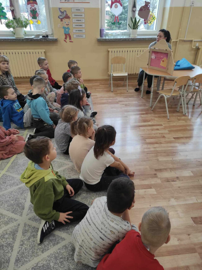 na zdjęciu widać salę przedszkolną, dzieci siedzą na dywanie, oglądają teatr kamishibai