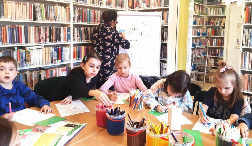 na zdjęciu widać sale biblioteczną i siedzące i rysujące dzieci