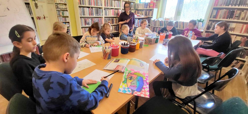 na zdjęciu widać dzieci siedzące przy stole w sali bibliotecznej