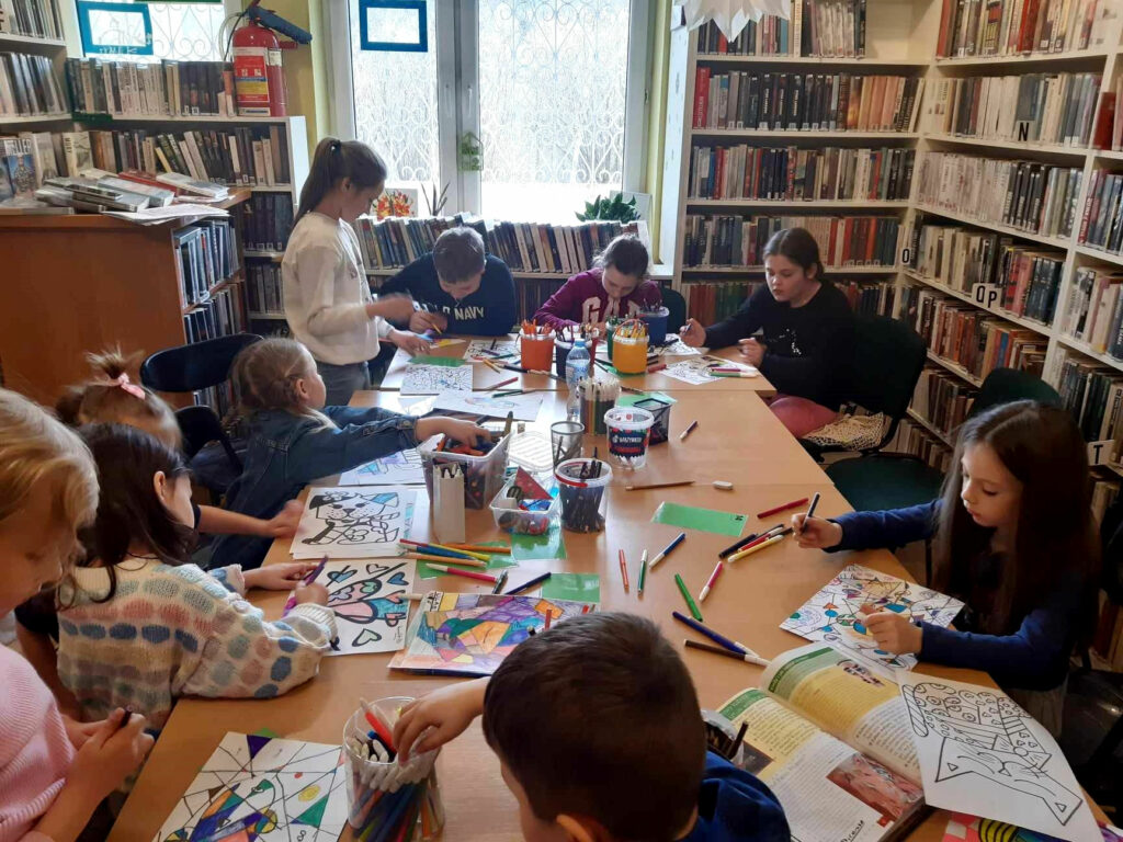 na zdjęciu widać dzieci siedzące przy stole w sali bibliotecznej