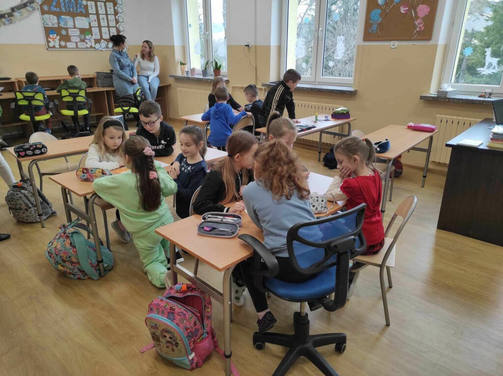 na zdjęciu widać salę szkolną, dzieci siedzą przy stolikach, biorą udział w zabawie