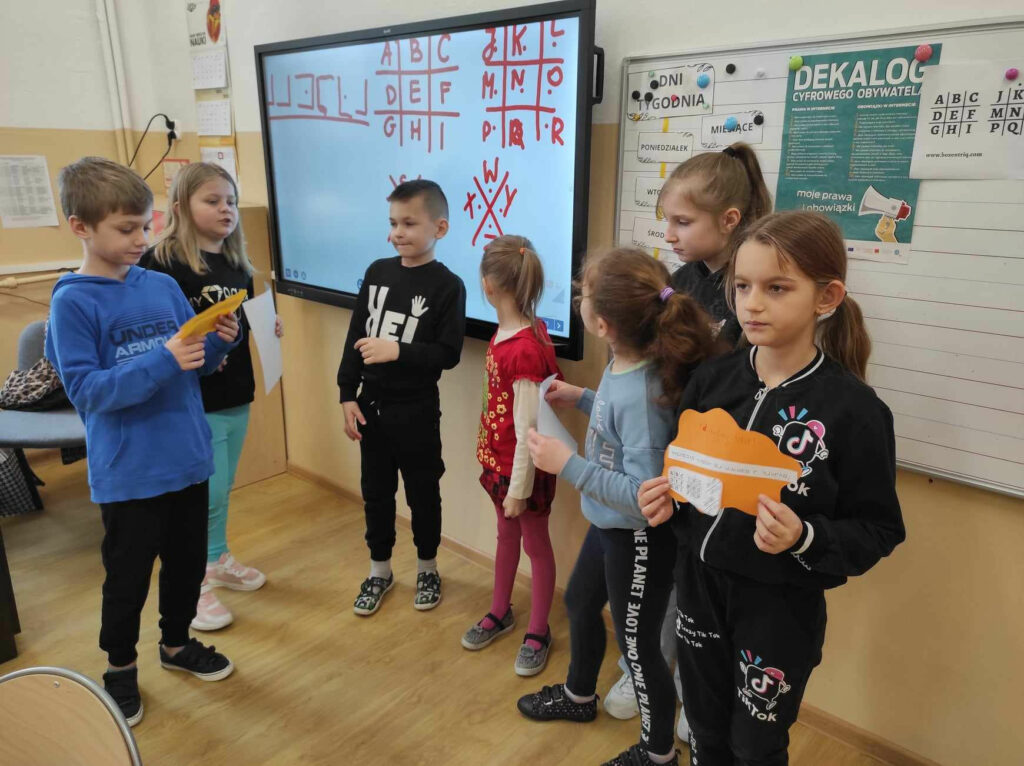 na zdjęciu widać salę szkolną, dzieci po rozwiązaniu zagadki prezentują rezultaty