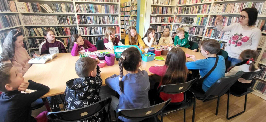 Na zdjęciu widać dzieci siedzące w sali bibliotecznej przy stole
