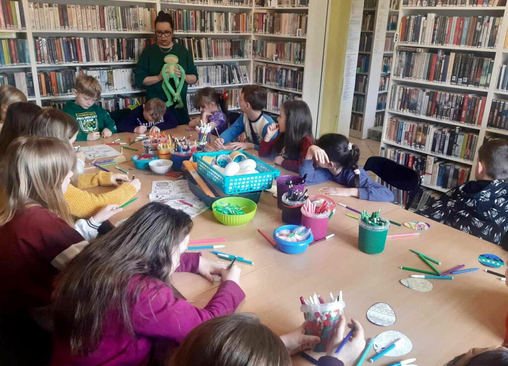 Na zdjęciu widać dzieci siedzące w sali bibliotecznej przy stole