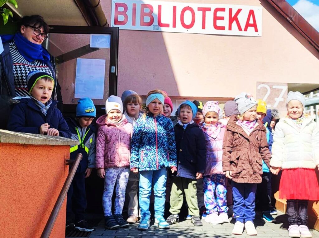 na zdjęciu widać dzieci stojące przed biblioteką