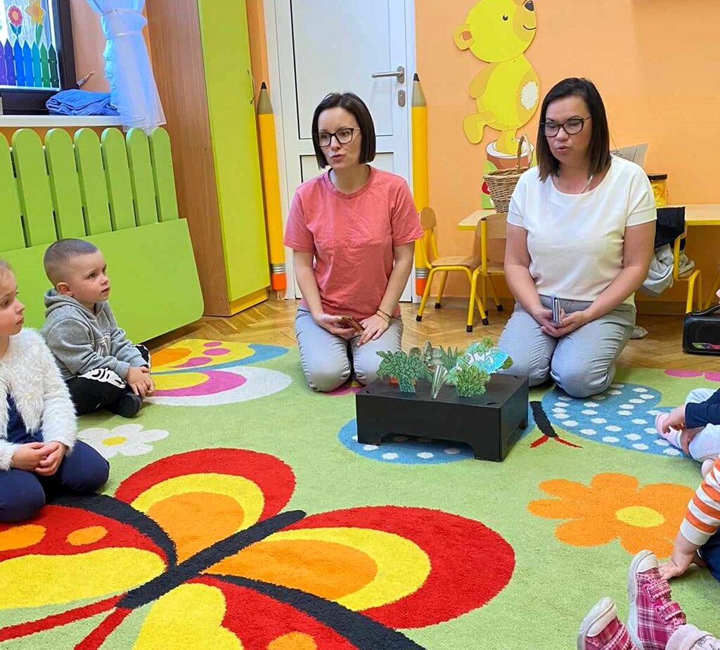 na zdjęciu widać kobiety oraz dzieci siedzące na kolorowym dywanie