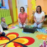 na zdjęciu widać kobiety oraz dzieci siedzące na kolorowym dywanie