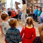 na zdjęciu widać dzieci stojące w kole oraz bibliotekarkę trzymającą papierowego konia