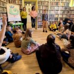 na zdjęciu widać dzieci i dwie bibliotekarki w sali bibliotecznej