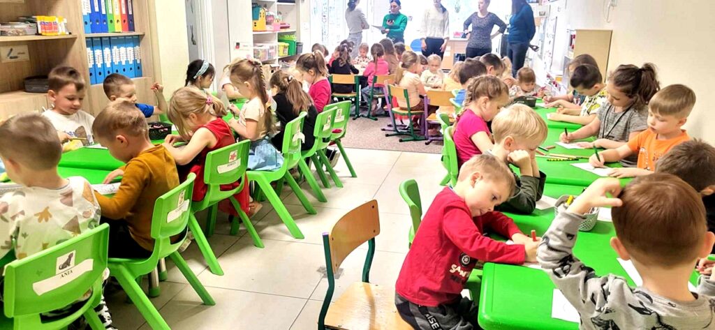 na zdjęciu widać dzieci siedzące przy zielonych stolikach