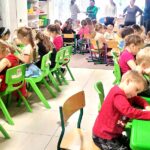 na zdjęciu widać dzieci siedzące przy zielonych stolikach