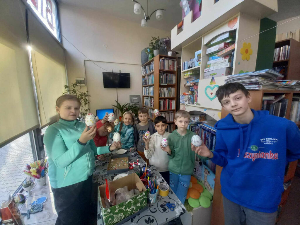 dzieci w bibliotece pokazują wykonane prace plastyczne