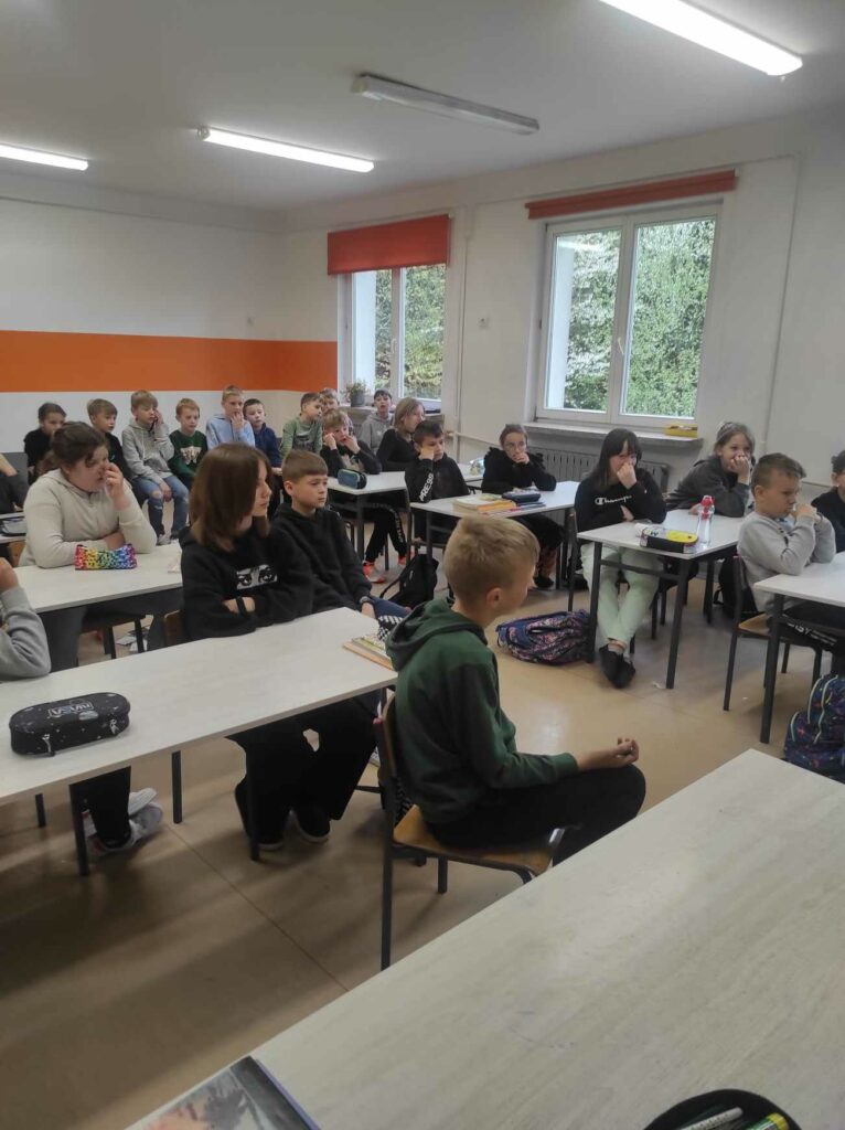 na zdjęciu widać salę szkolną, uczniowie siedzą przy stolikach, słuchają opowiadania