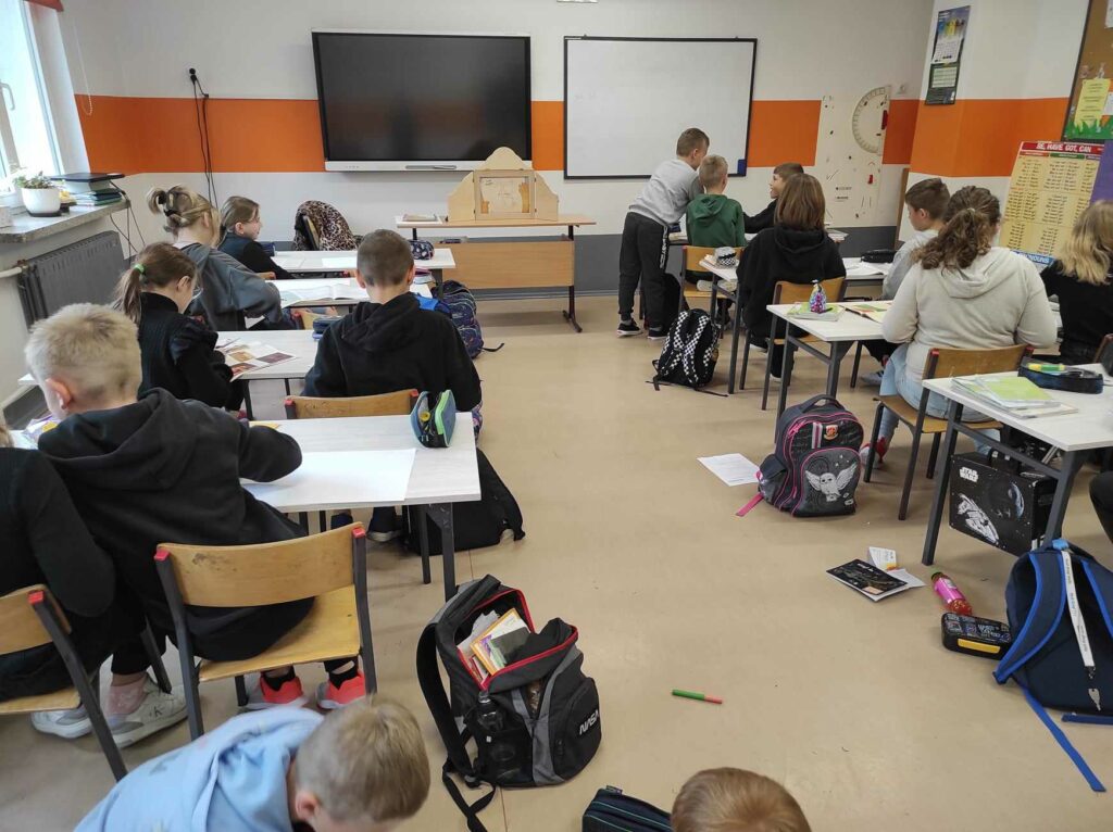 na zdjęciu widać salę szkolną, uczniowie siedzą przy stolikach, wykonują prace