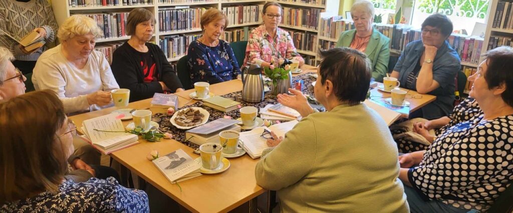 na zdjęciu panie siedzące wokół stołu w sali bibliotecznej