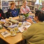 na zdjęciu panie siedzące wokół stołu w sali bibliotecznej