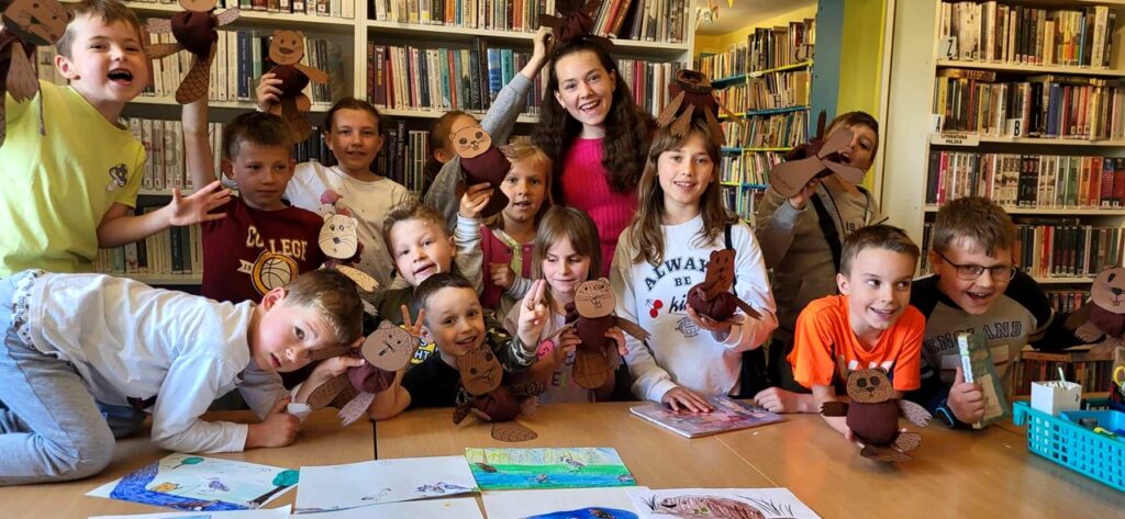 Na zdjęciu widać dzieci w sali bibliotecznej przy stole prezentują swoje prace.