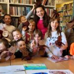 Na zdjęciu widać dzieci w sali bibliotecznej przy stole prezentują swoje prace.