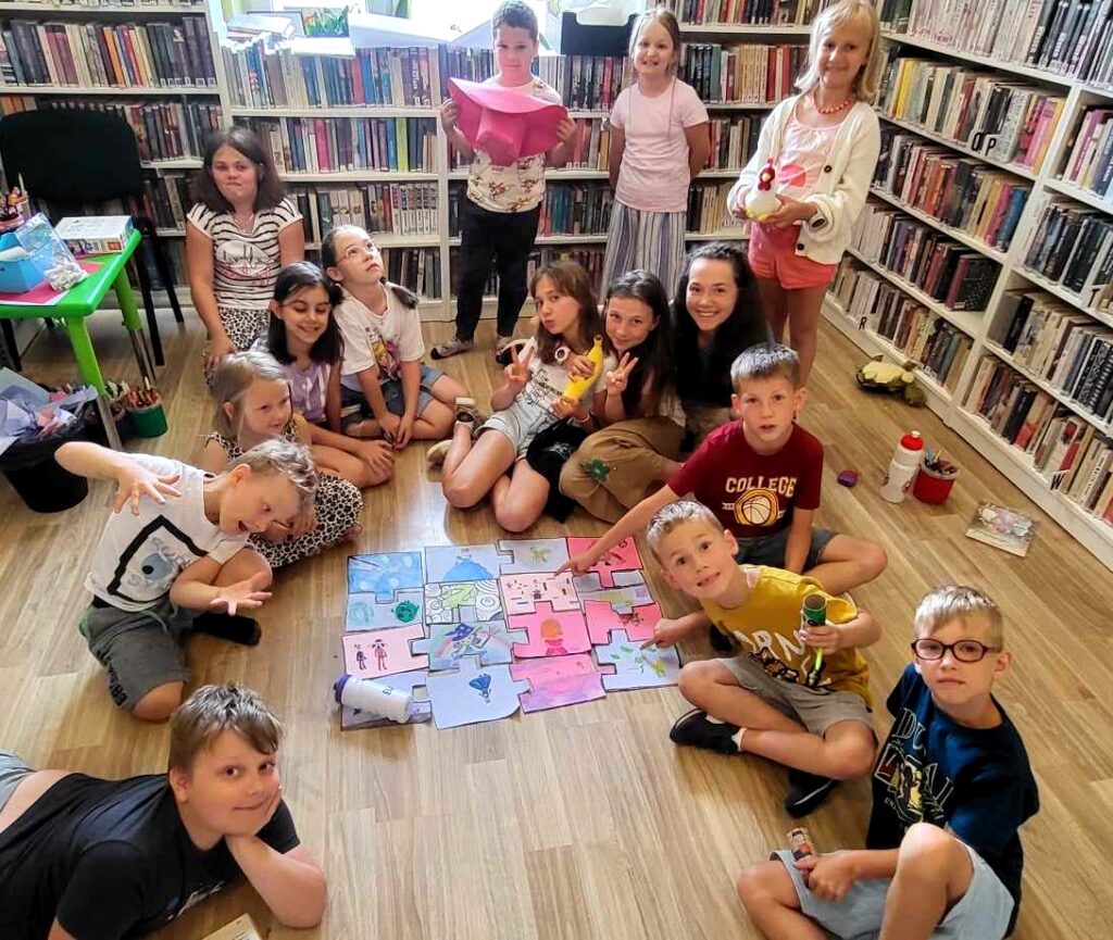 na zdjęciu widać dzieci siedzące na podłodze w sali bibliotecznej