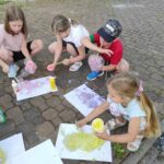 na zdjęciu widać podwórko przy bibliotece, dzieci malują papier kolorową pianą