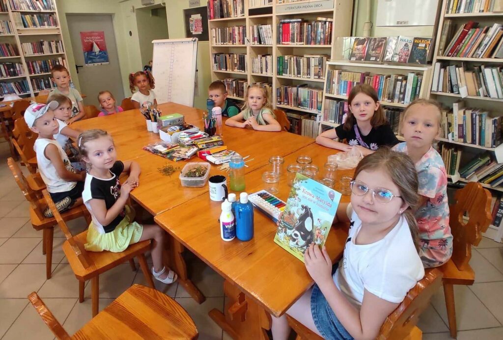 na zdjęciu widać salę biblioteczną, dzieci siedzą przy stole