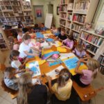 na zdjęciu widać salę biblioteczną, dzieci siedzą przy stole, wykonują pracę plastyczną