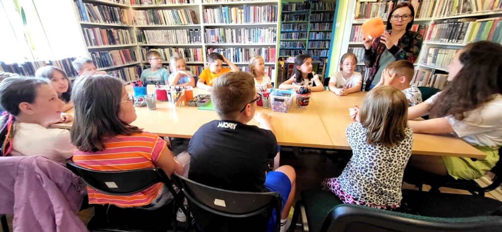 na zdjęciu widać dzieci siedzące przy stole w sali bibliotecznej