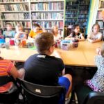 na zdjęciu widać dzieci siedzące przy stole w sali bibliotecznej