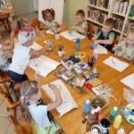 na zdjęciu widać salę biblioteczną, dzieci siedzą przy stole, wykonują pracę plastyczną