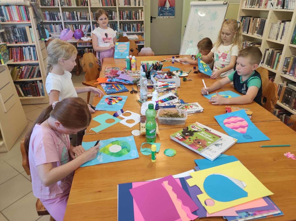 na zdjęciu widać salę biblioteczną, dzieci siedzą przy stole, wykonują zadanie