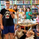 na zdjęciu widać dzieci stojące w sali bibliotecznej na tle regałów z książkami.