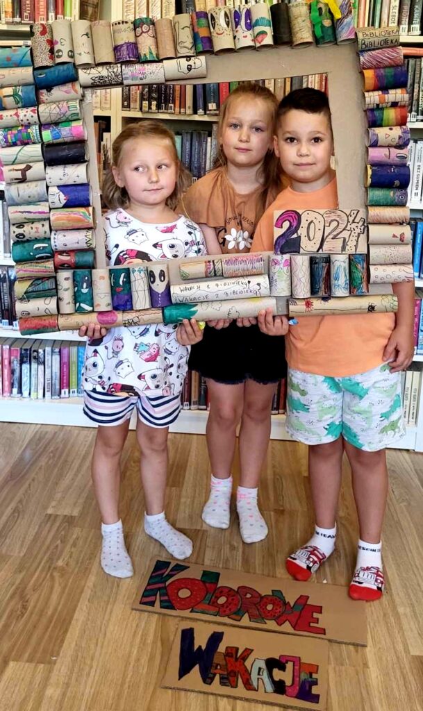 na zdjęciu widać dzieci pozujące do zdjęcia na tle regalu z książkami