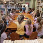 na zdjęciu widać salę biblioteczną, dzieci siedzą przy stole, bawią się w kalambury