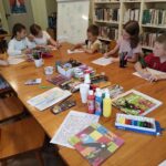 na zdjęciu widać salę biblioteczną, dzieci siedzą przy stole, po wysłuchaniu książki wykonują zadanie