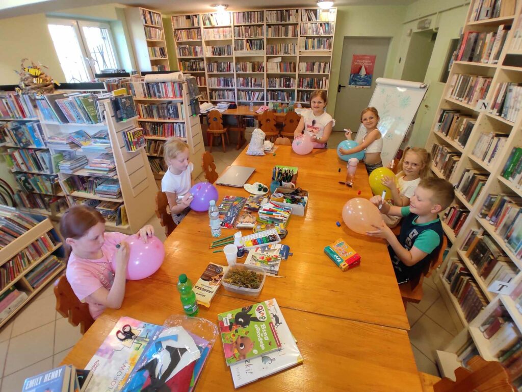 na zdjęciu widać salę biblioteczną, dzieci siedzą przy stole, wykonują prace plastyczne