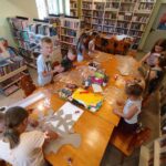 na zdjęciu widać salę biblioteczną, przy stole siedzą dzieci, projektują witraże