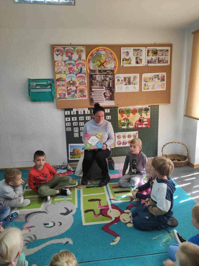 na zdjęciu widać dzieci siedzące na dywanie, oglądają książki