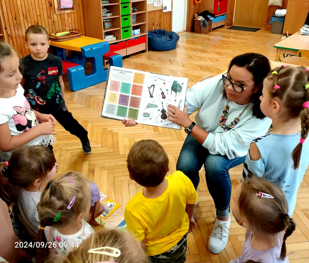 na zdjęciu widać dzieci oraz kobieta pokazującą im książkę