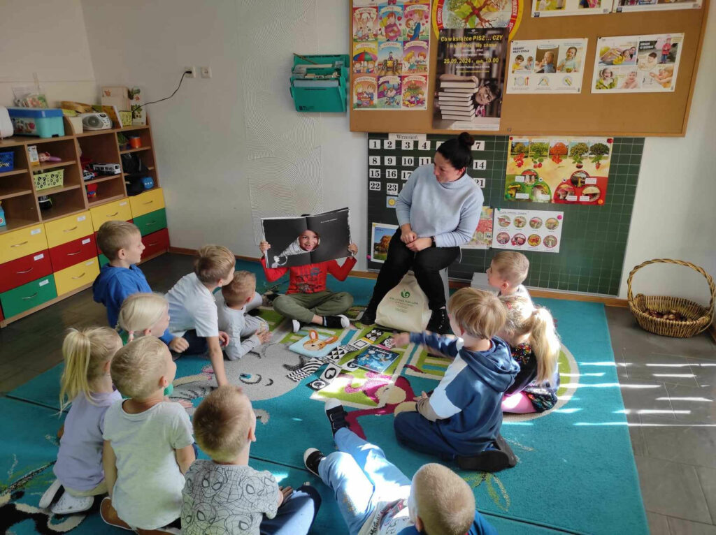 na zdjęciu widać dzieci siedzące na dywanie, oglądają książki