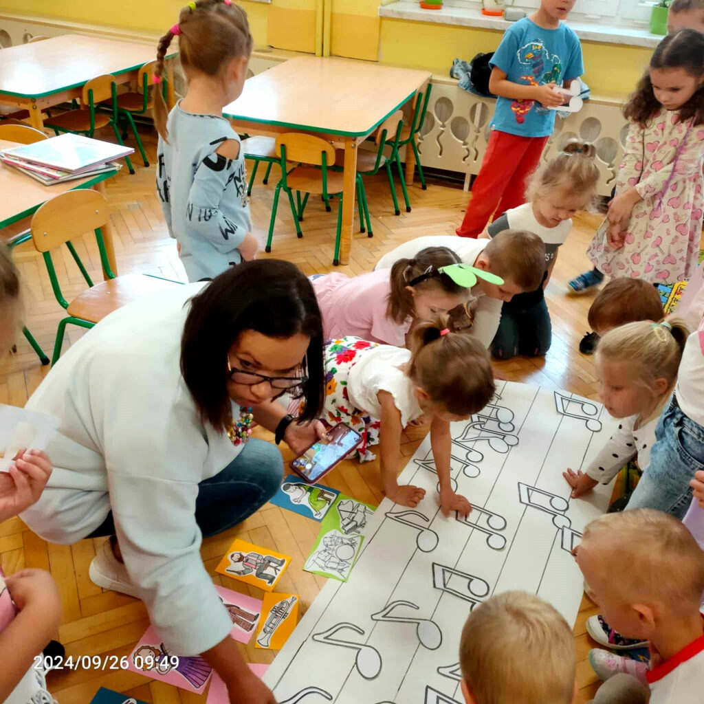 na zdjęciu widać kobietę oraz dzieci układające obrazki na ziemi