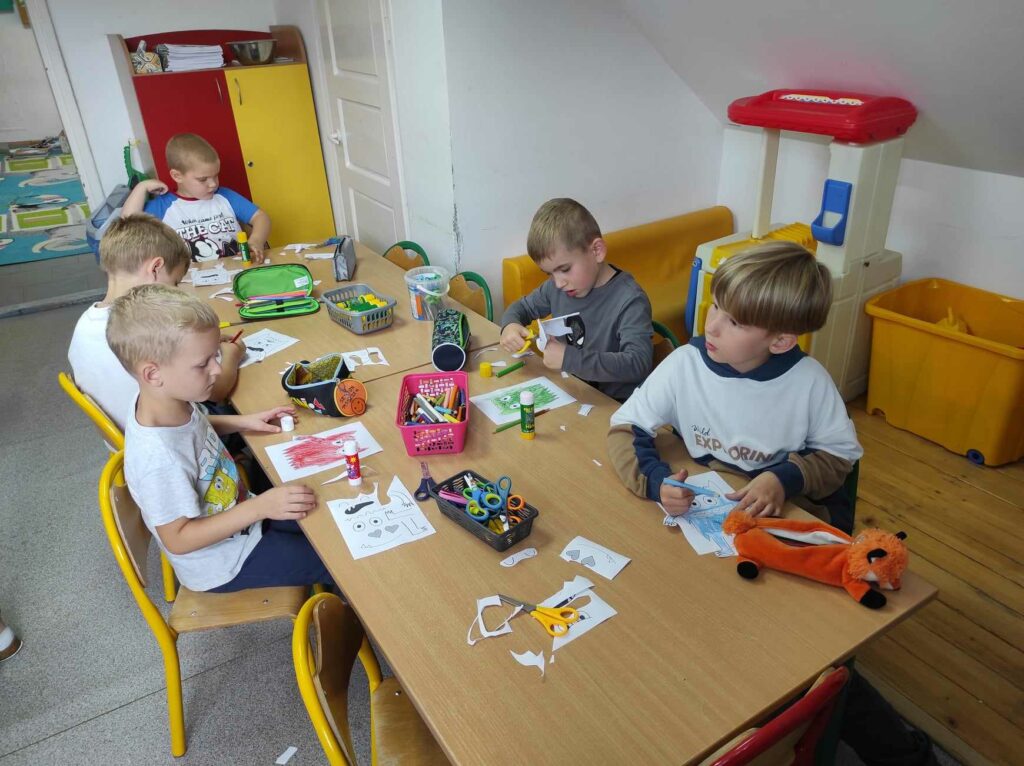 na zdjęciu widać dzieci, siedzą przy stolikach i wykonują pracę plastyczną