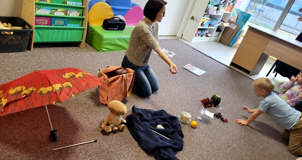 na zdjęciu różne przedmioty poukładane na ziemi oraz siedzącą kobietę