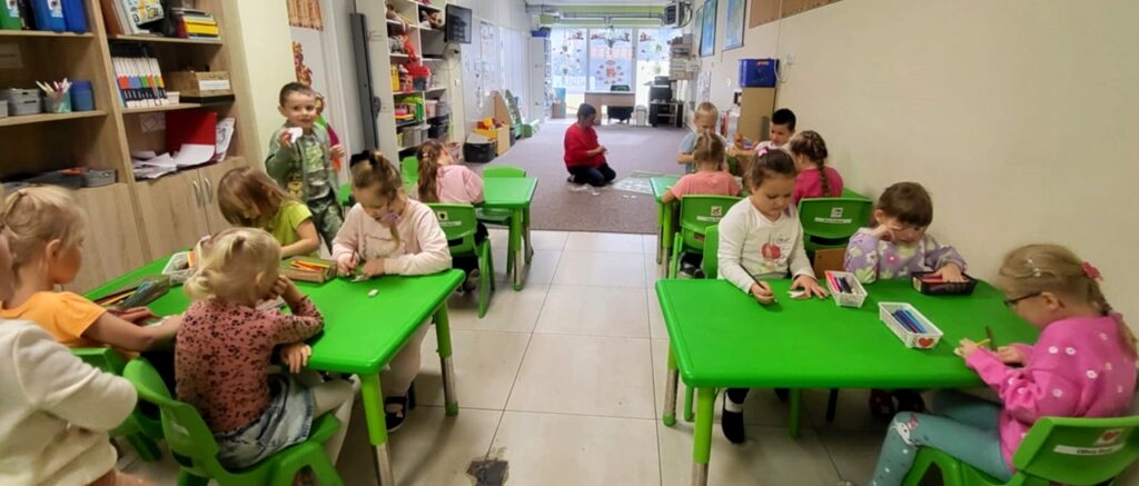 na zdjęciu widać dzieci siedzące przy zielonych stolikach